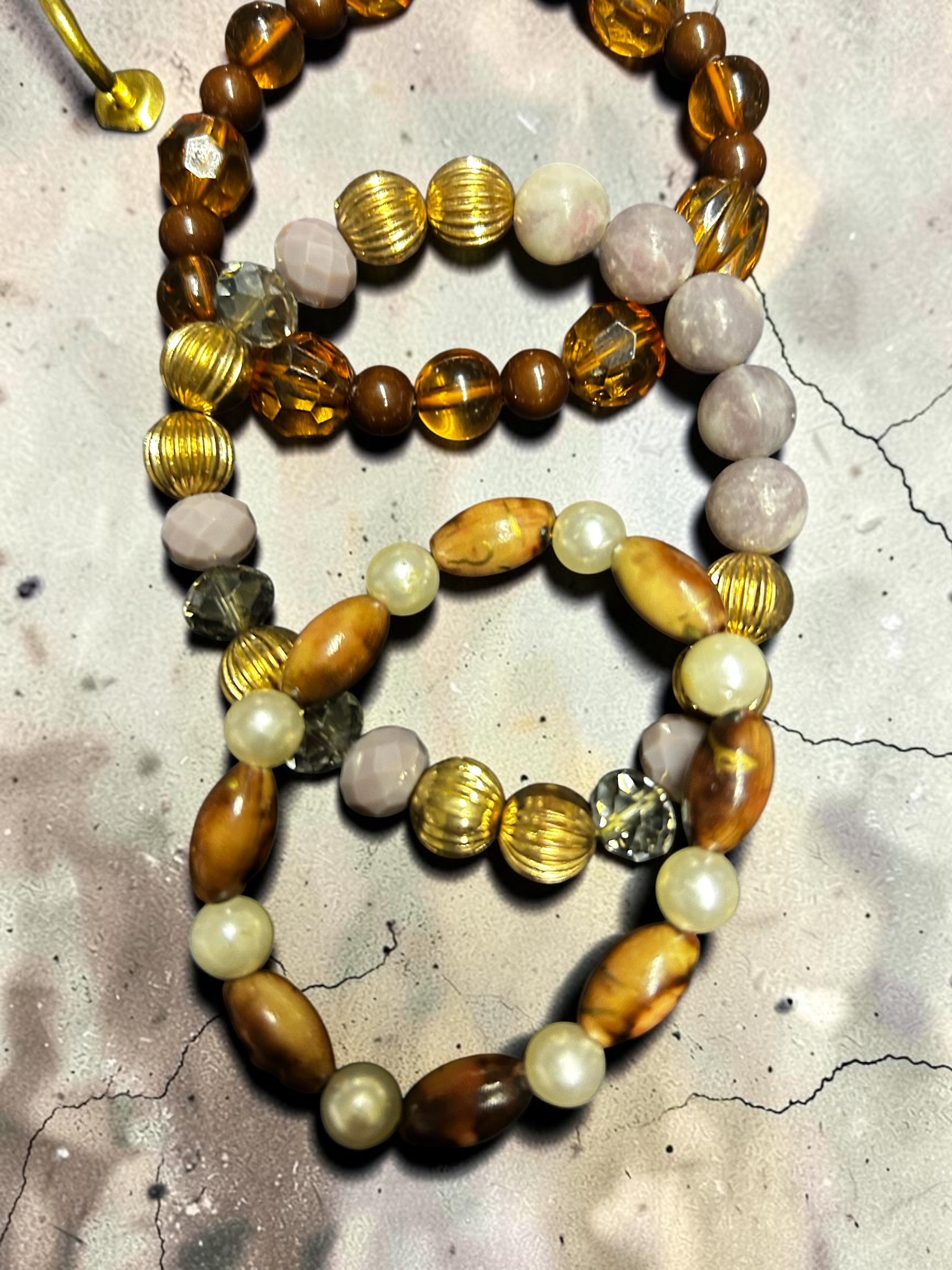 M.C’s set of three stretch bracelets featuring amber glass, lavender stones, wood-grain beads, and cream pearls.