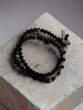 M.C’s multi-strand wrap bracelet featuring faceted black crystal beads and gold-tone metal accents on a concrete block.