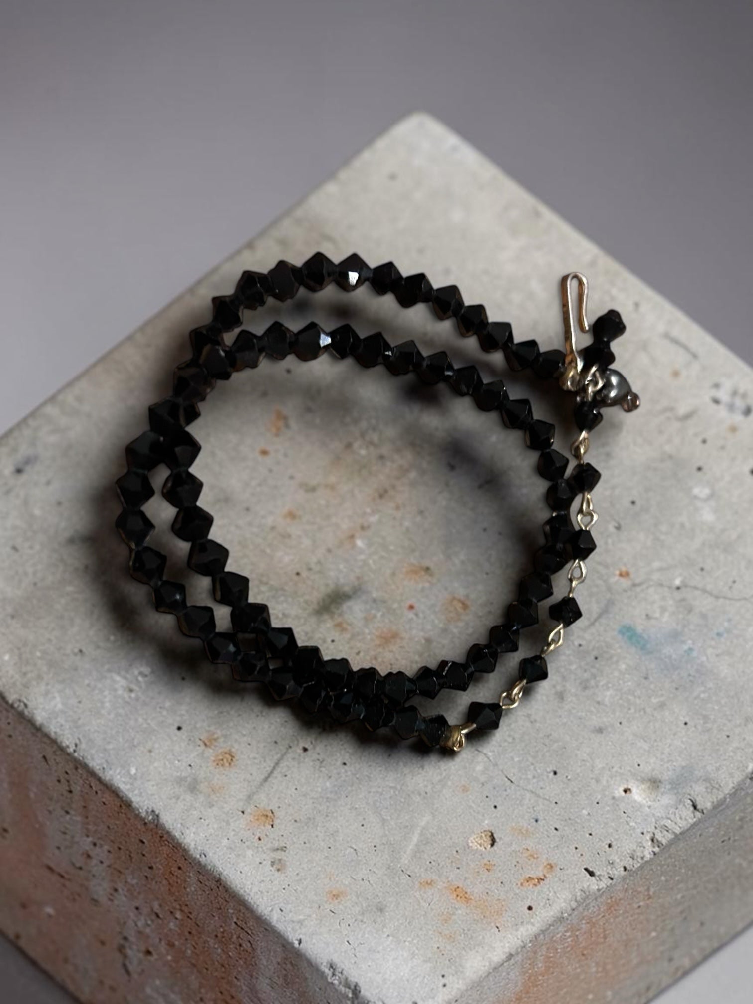 M.C’s multi-strand wrap bracelet featuring faceted black crystal beads and gold-tone metal accents on a concrete block.