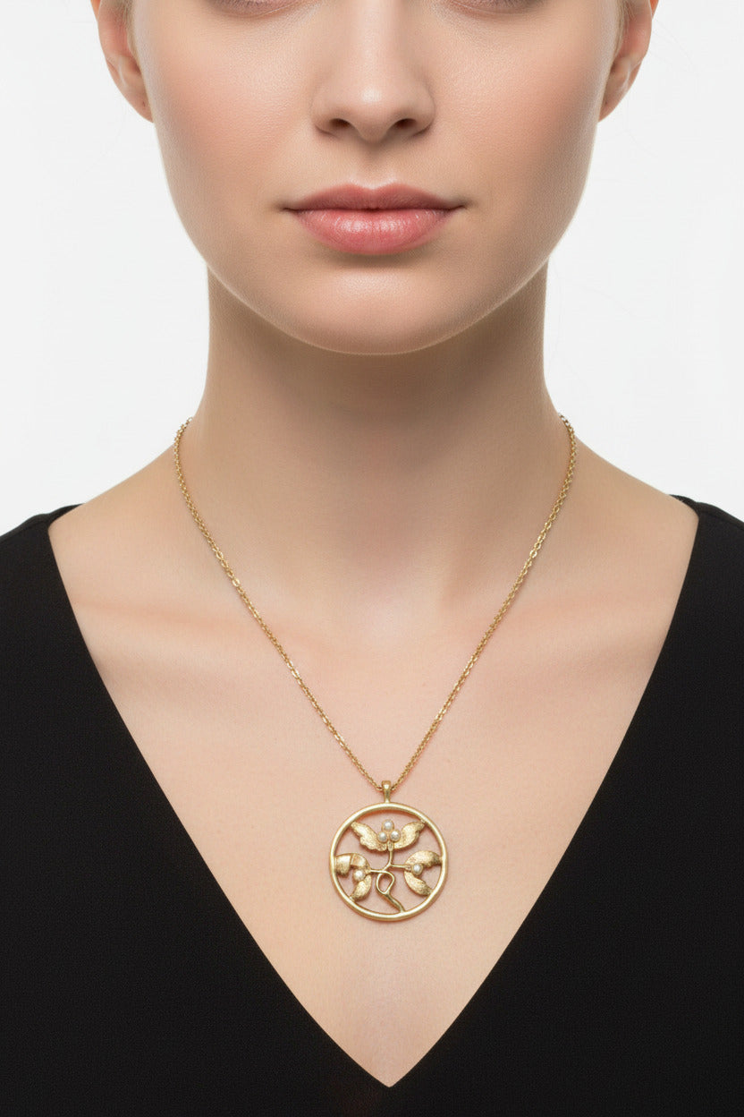 M.C’s vintage-inspired circular pendant necklace featuring a brushed gold-tone botanical design with faux pearls.