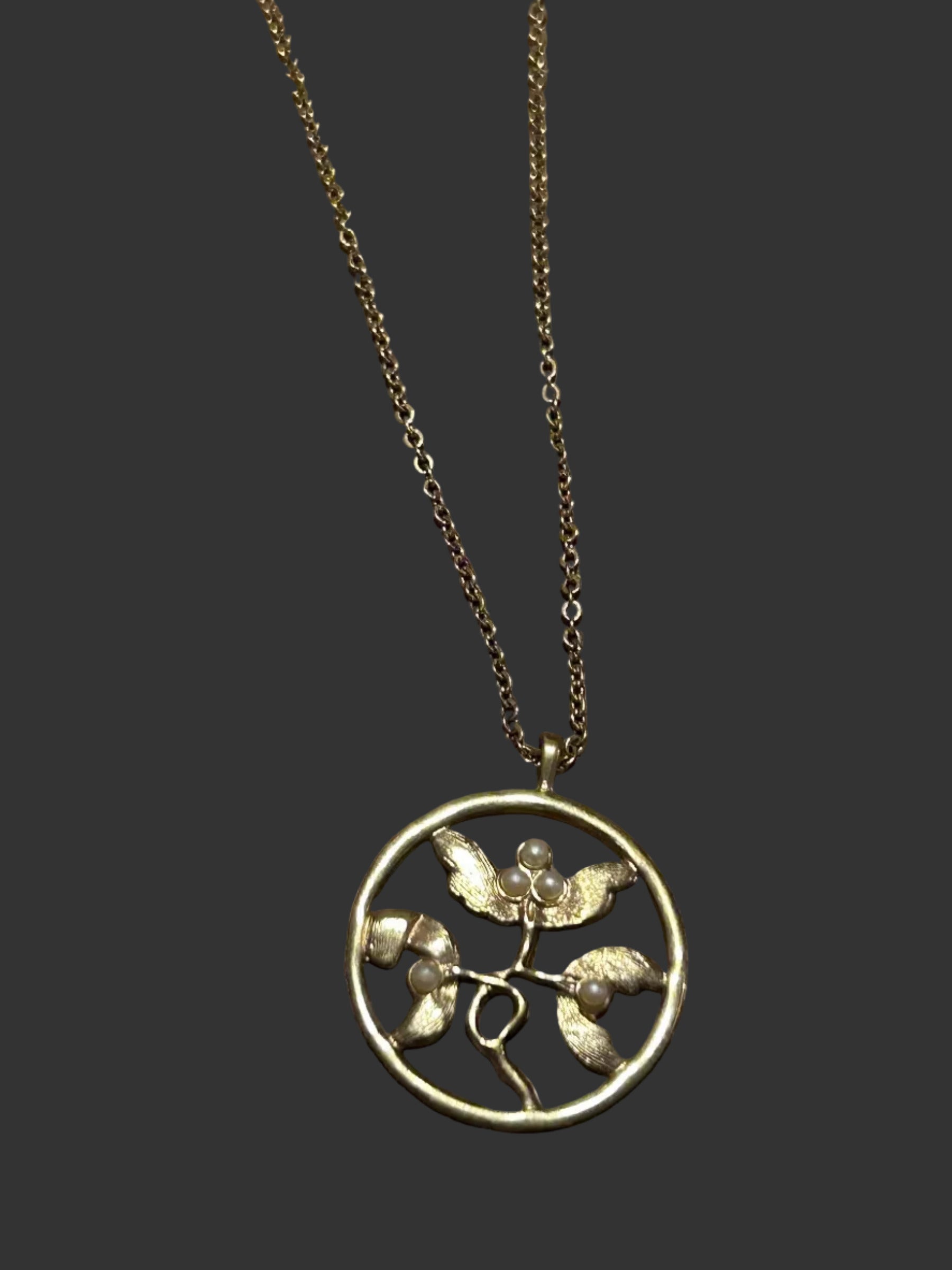 M.C’s vintage-inspired brushed gold circular pendant necklace featuring botanical leaf motifs and faux pearl accents.