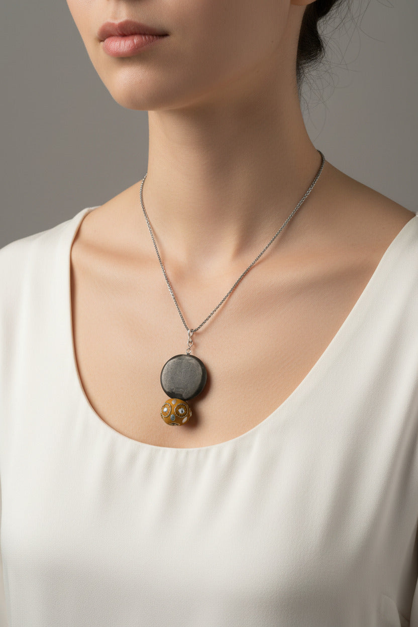 M.C’s decorative pendant necklace featuring a matte dark grey disc and a mustard beaded charm on a silver-tone chain.