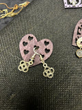 M.C’s decorative metal drop earrings featuring an intricate open-work four-leaf clover design on a heart display card.