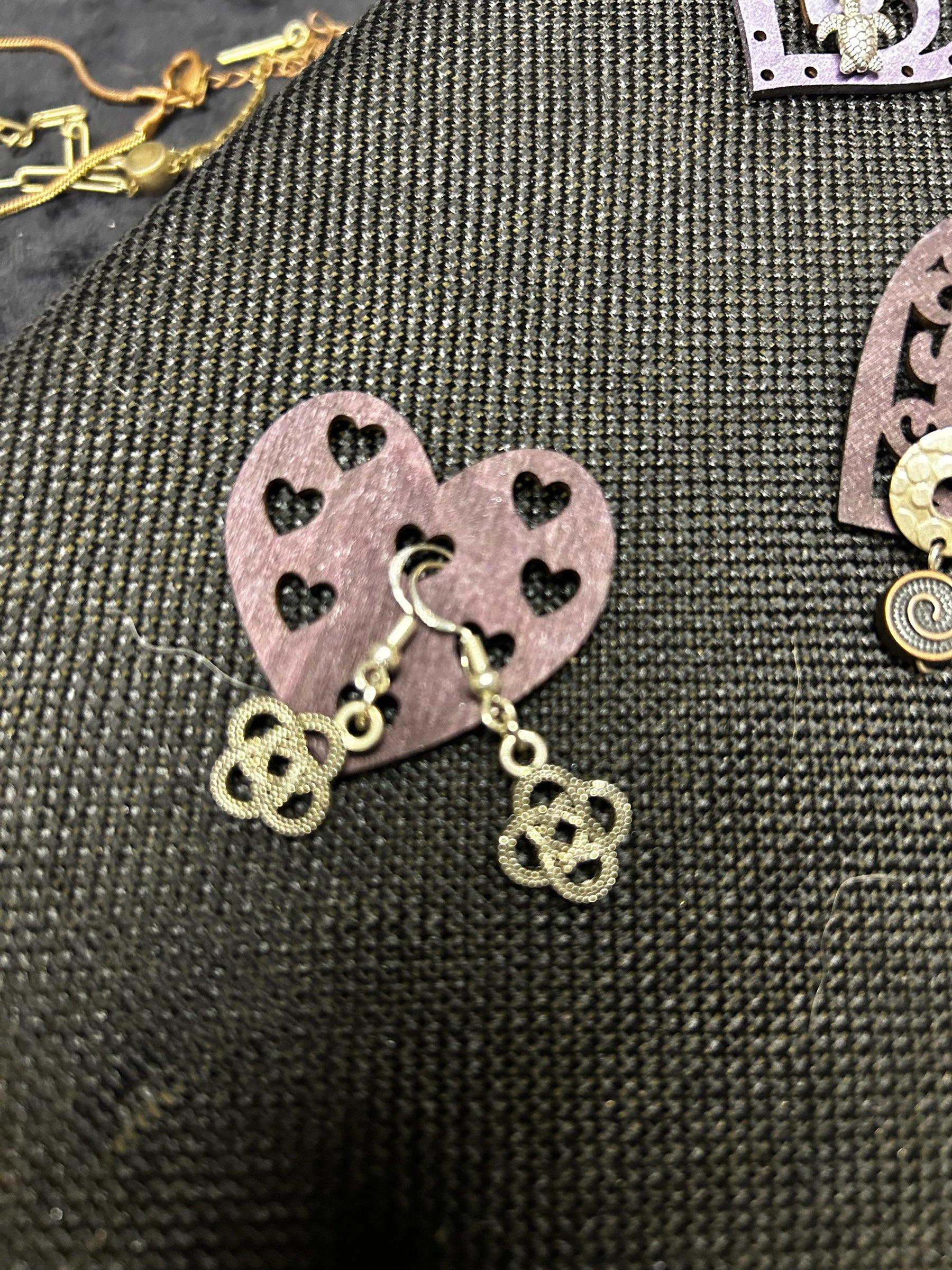 M.C’s decorative metal drop earrings featuring an intricate open-work four-leaf clover design on a heart display card.