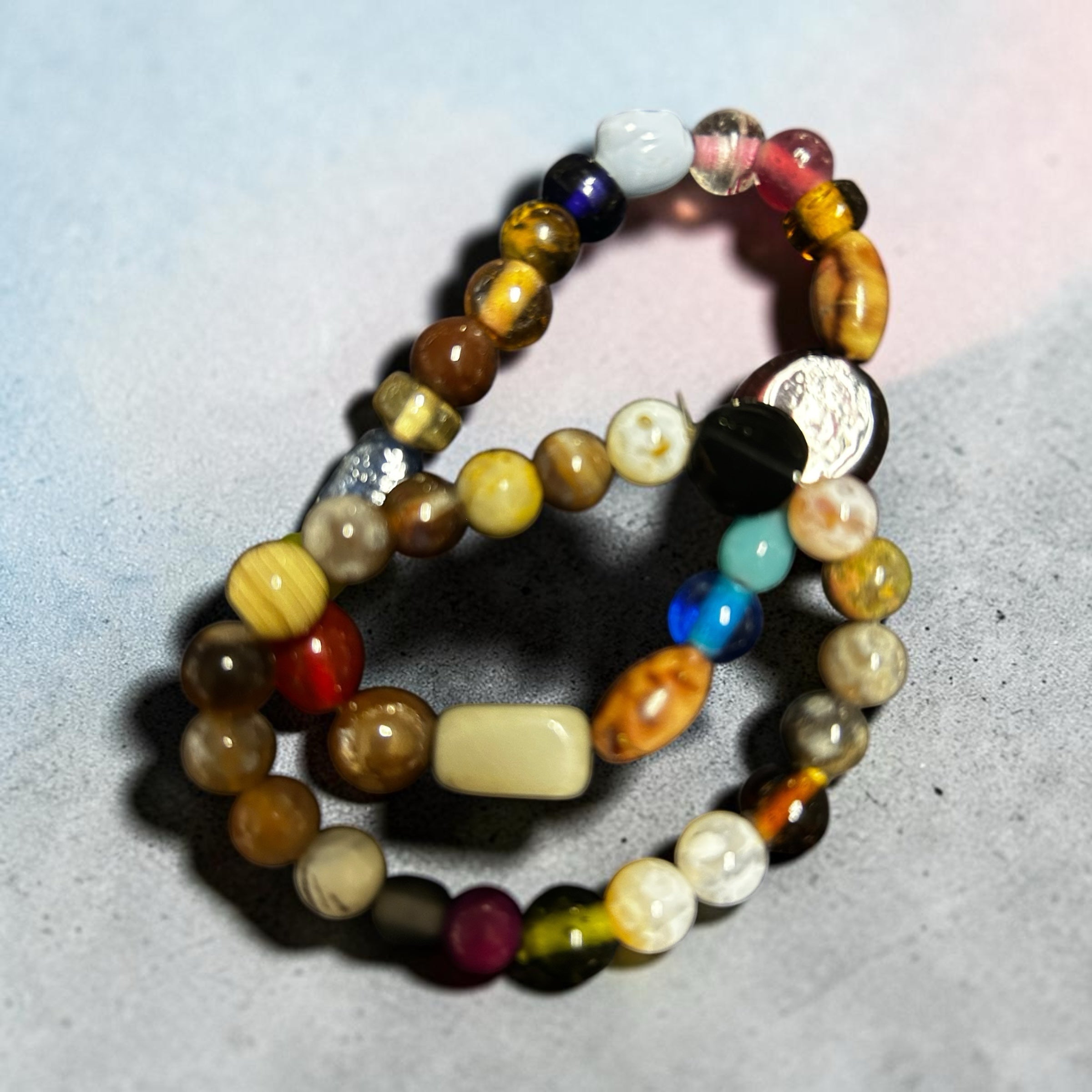 M.C’s handcrafted stretch bracelet set featuring polished multi-colored gemstone beads in earthy, blue, and red tones.
