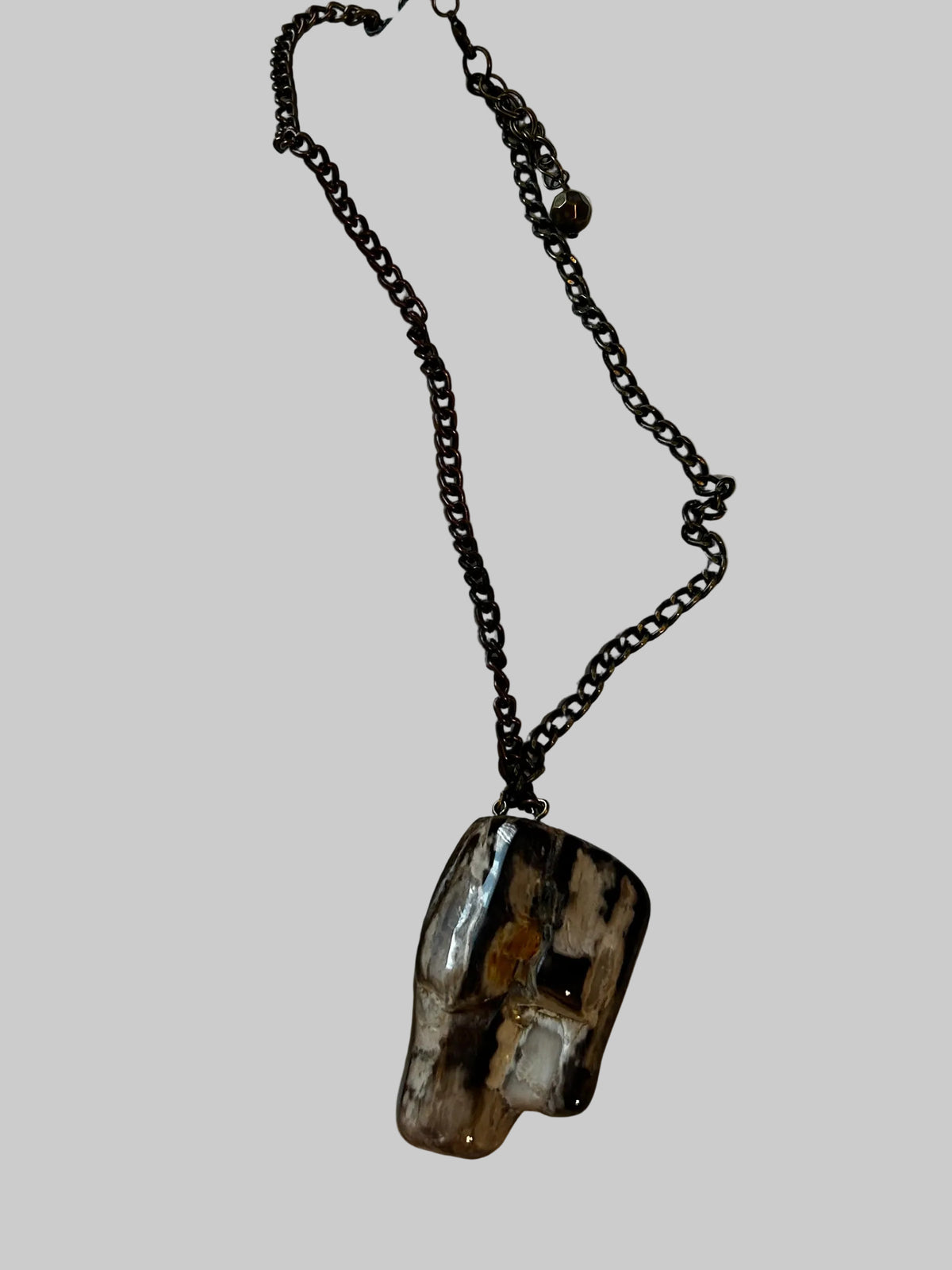 M.C’s petrified wood pendant necklace with a polished, irregular stone in black and brown on a dark metal chain.