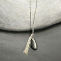 M.C’s decorative pendant necklace featuring a smooth dark river stone and a shimmering silver-tone tassel on a thin chain.