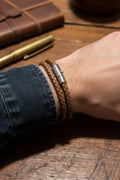 M.C’s tan braided leather men's bracelet with a polished stainless steel magnetic clasp on a wooden surface.